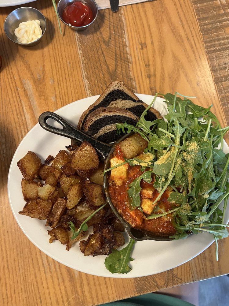 Vegan eggs in purgatory in a cast-iron skillet with home fries, arugula and toast